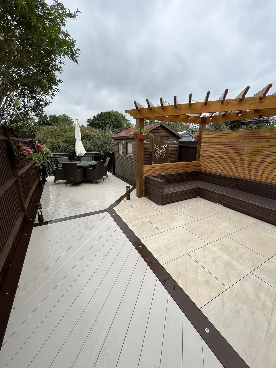 Pale garden paving beside decking, a timber pergola and built-in seating