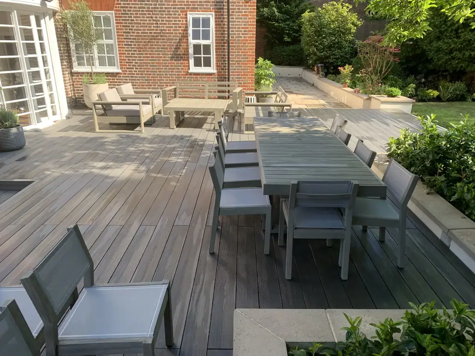 A table and seating arranged on a deck beside planted borders