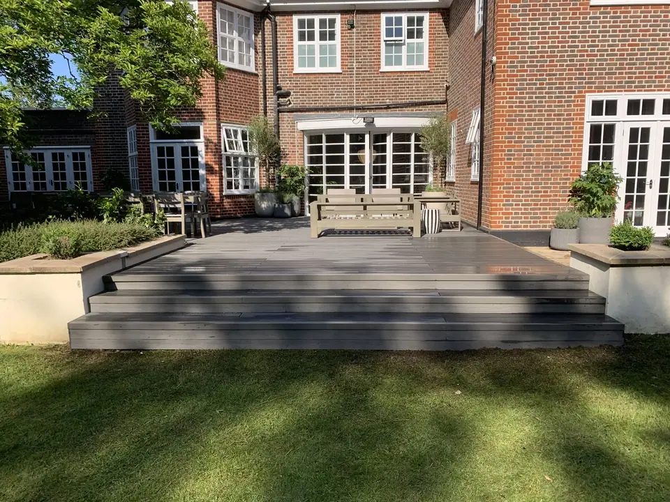 A broad garden deck and wide steps between a brick house and lawn