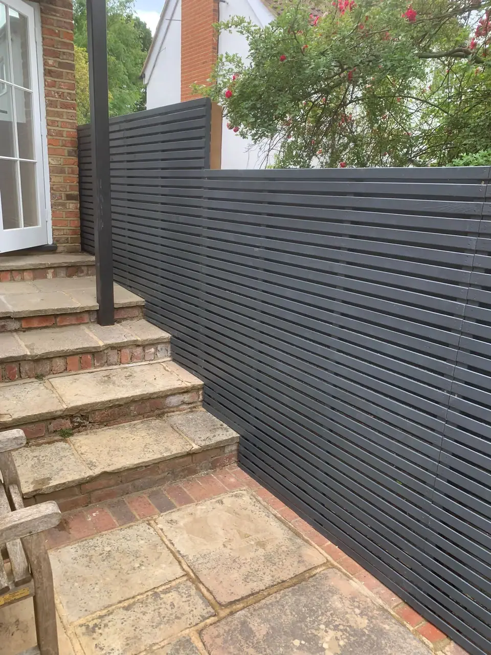 Dark horizontal slat fencing beside steps and a planted boundary