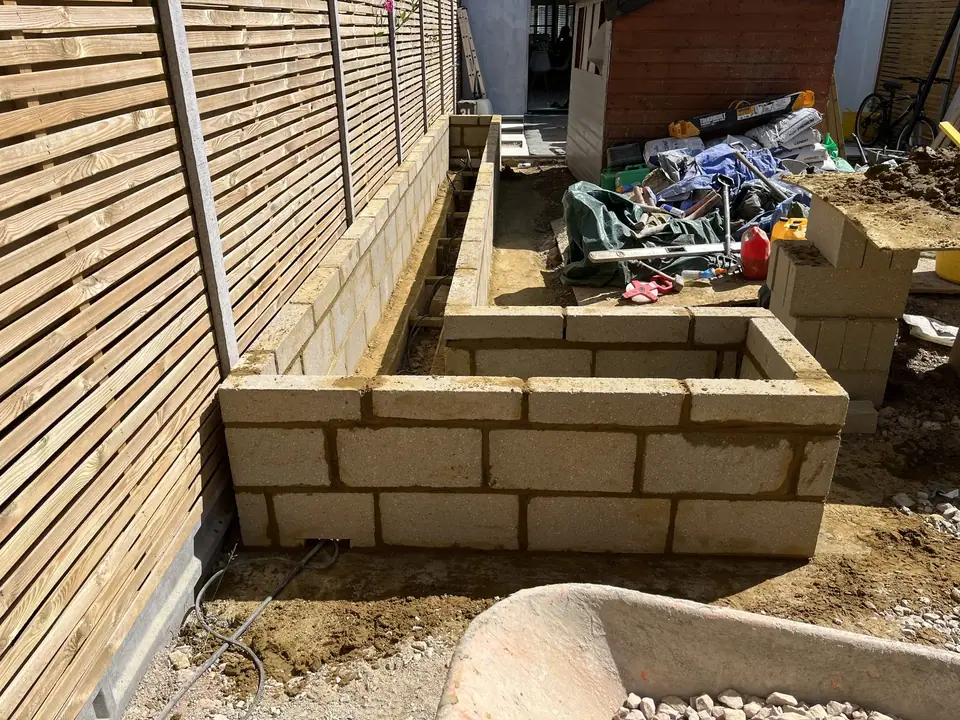 Masonry planter walls under construction beside slatted fencing