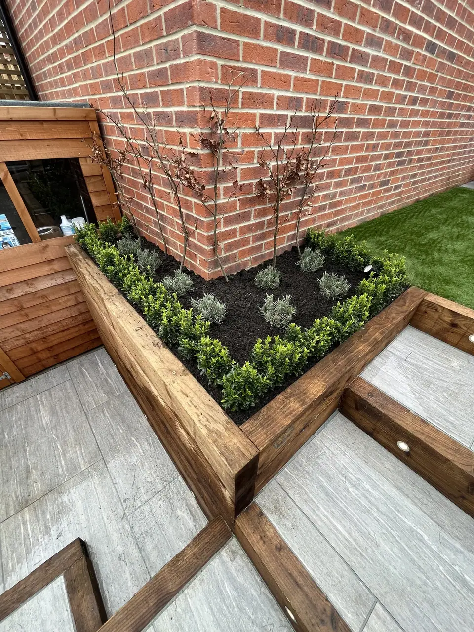 Timber-edged planted bed beside pale garden steps and a brick wall