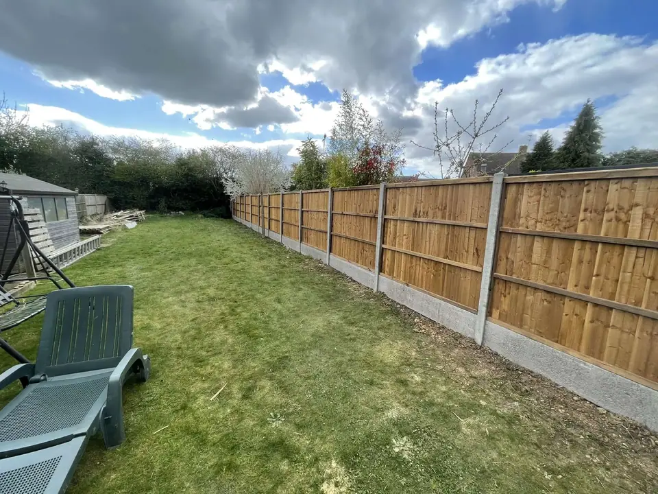 A long run of timber fence panels with concrete posts beside a lawn